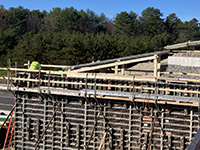 Worker oversees form and rebard work atop concrete wall.